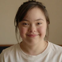 Hanna, a young woman with Down syndrome, smiling softly in warm home light