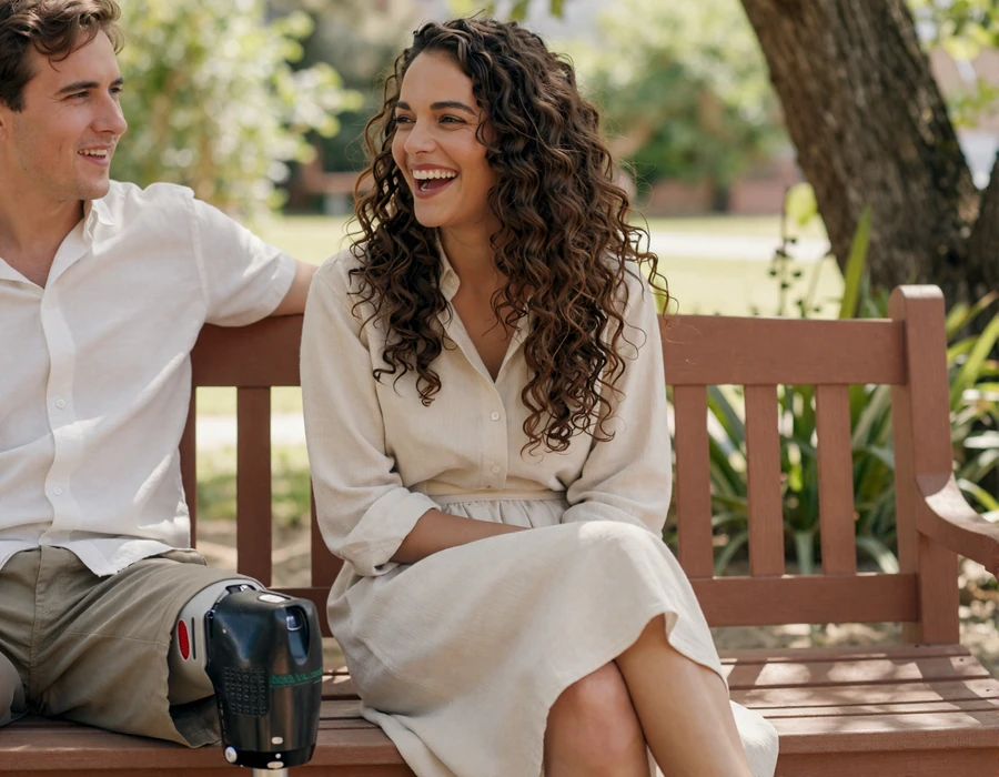 Mixed-race woman below-knee amputee laughing with her partner on a sunlit garden bench - authentic amputee dating connection