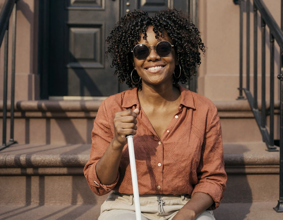 Naomi, a blind woman with a white cane, smiling on a sunlit stoop - blind people dating on easy dating